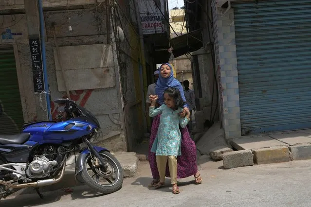 A Muslim girl wearing hijab plays with a younger girl next to closed shops run by Muslims during a day long general strike called by Karnataka state's Muslim chief priest to protest against the court verdict that upheld the ban on wearing hijab in schools, in Bengaluru, Thursday, March 17, 2022. An Indian court ruling upholding a ban on Muslim students wearing head coverings in schools has sparked criticism from constitutional scholars and rights advocates amid concerns of judicial overreach regarding religious freedoms. (Photo by Aijaz Rahi/AP Photo)