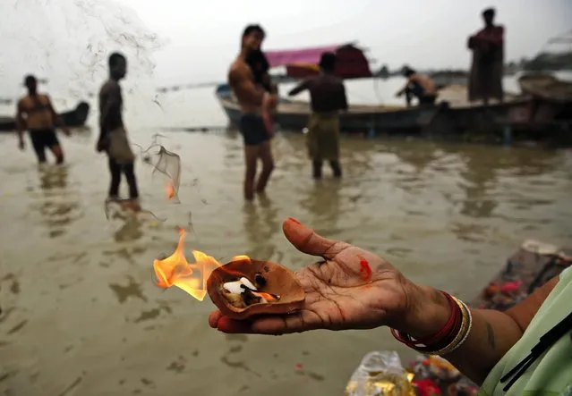 A woman prays as others take holy dips at Sangam, the confluence of the Rivers Ganges, Yamuna the mythical Saraswati, on the occasion of Guru Purnima, or full moon day dedicated to the Guru, in Allahabad, India, Friday, July 31, 2015. (Photo by Rajesh Kumar Singh/AP Photo)