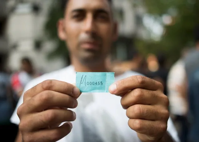 A newly arrived refugee holds a number that has been allocated to him by the authority in order to get accommodation in front of the Berlin State Office for Health and Social Affairs where he waits with other migrants to apply for asylum in Berlin, August 10, 2015. (Photo by Stefanie Loos/Reuters)