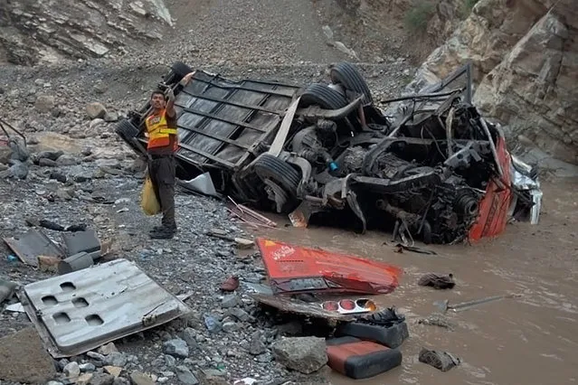 In this photo provided by Baluchistan's rescue department, a rescue worker stands next to the wreck of a passenger bus, in Zhob, Baluchistan province, in southwest Pakistan, Sunday, July 3, 2022. An official said the passenger bus slid off a mountain road and fell 200 feet (61 meters) into a ravine in heavy rain killing at least 18 people and injuring some 12 others. (Photo by Baluchistan Rescue Department via AP Photo)