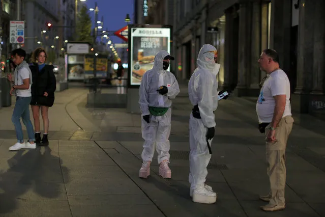 People wearing protective clothes talk with a man at the Gran Via avenue in downtown in Madrid, Spain, Saturday, March 14, 2020. (Photo by Manu Fernandez/AP Photo)