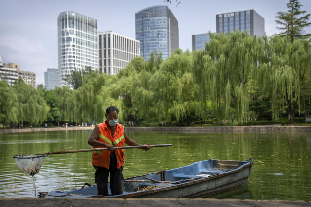 A maintenance worker wearing a face mask skims leaves from a pond at a public park in Beijing, Tuesday, July 26, 2022. (Photo by Mark Schiefelbein/AP Photo)
