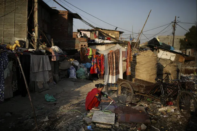 In this Tuesday, March 17, 2020 photo, a woman fills a plastic bottle with pipe water next to a drain filled with plastic and other filth at a slum in New Delhi, India. (Photo by Altaf Qadri/AP Photo)