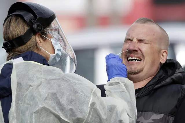 A man reacts as a medical staffer tests shoppers who volunteered at a pop-up community COVID-19 testing station at a supermarket carpark in Christchurch, New Zealand, Friday, April 17, 2020. New Zealand is into week four of a 28-day lockdown in a bid to stop the spread of the new coronavirus. (Photo by Mark Baker/AP Photo)