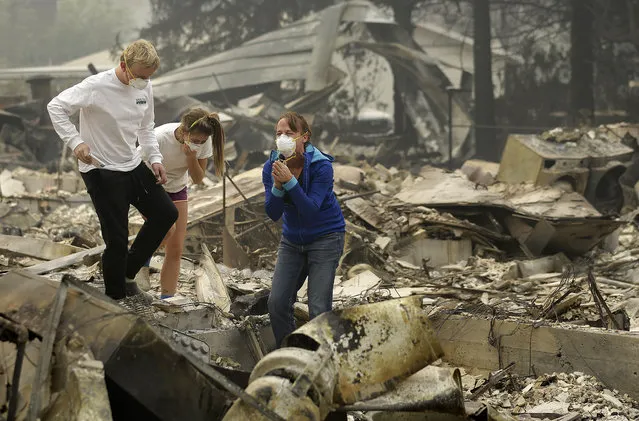 Mary Caughey, center in blue, reacts with her son Harrison, left, after finding her wedding ring in debris at her home destroyed by fires in Kenwood, Calif., Tuesday, October 10, 2017. (Photo by Jeff Chiu/AP Photo)