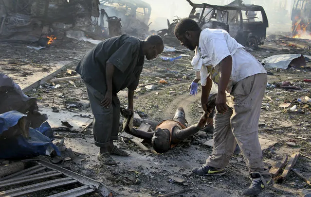 Somalis remove the body of a man killed in a blast in the capital Mogadishu, Somalia Saturday, October 14, 2017. (Photo by Farah Abdi Warsameh/AP Photo)