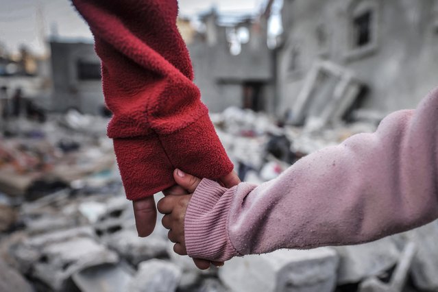 People hold hands as they inspect the damage on buildings destroyed during Israeli bombardment in Rafah on the southern Gaza Strip on December 29, 2023, amid the ongoing battles between Israel and the Palestinian militant group hamas. (Photo by AFP Photo)