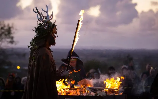 A man representing the Winter King holds a flaming sword as he takes part in a ceremony as they celebrate Samhain at the Glastonbury Dragons Samhain Wild Hunt 2017 in Glastonbury on November 4, 2017 in Somerset, England. To celebrate Samhain, the Glastonbury Dragons, alongside Gwythyr Ap Greidal, the Summer King and the Winter King, Gwyn Ap Nudd, were paraded through the town to the lower slopes of Glastonbury Tor where the event was marked with ritual theatre, dancing and a fire to honour the dead. The Celtic festival of Samhain, which was later adopted by Christians and became Halloween, is a very important date in the Pagan calendar as it marks the division of the year between the lighter half (summer) and the darker half (winter). Pagans believe at Samhain, the division between this world and the otherworld was at its thinnest, allowing spirits to pass through. Many of the traditions of this ancient Celtic feast of the dead were later incorporated into the Christian calendar and Irish immigrants to America in the 19th century carried their customs, such as the wearing of costumes and masks to ward of harmful spirits and the harvest tradition of carving pumpkins, which have now blended into modern day Hallowee. (Photo by Matt Cardy/Getty Images)