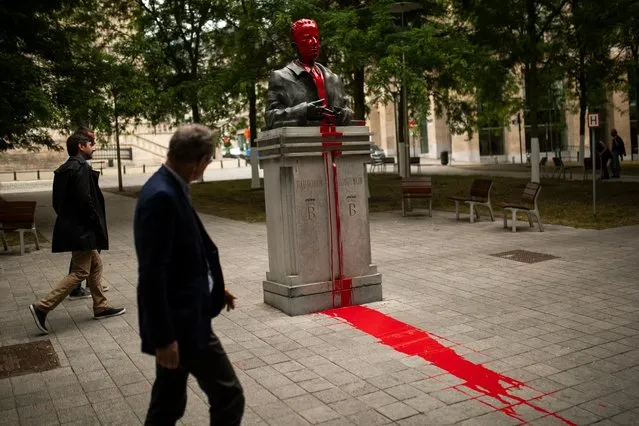 People walk past a bust of former Belgium's King Baudouin being vandalised and covered in red paint in Brussels, Friday, June 12, 2020. The red paint vandalism of the statue forms part of anti-racism protests in Brussels. (Photo by Francisco Seco/AP Photo)