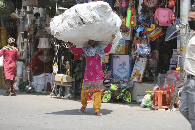 A laborer carries a load of plastic toys at a market in Jammu, India, Friday, June 19, 2020. India is the fourth hardest-hit country by the COVID-19 pandemic in the world after the U.S., Russia and Brazil. (Photo by Channi Anand/AP Photo)