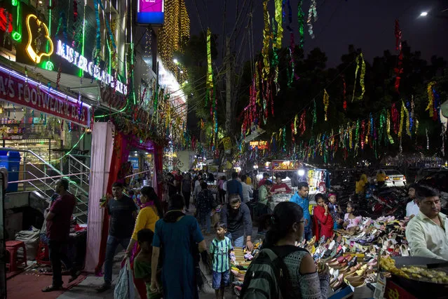 A boy stands and watches as people shop for decorative items, clay lamps and electric lights to decorate their homes ahead of Diwali festival in New Delhi, India, Thursday, October 20, 2022. Diwali, the festival of lights, will be celebrated on Oct. 24. (Photo by Bhumika Saraswati/AP Photo)