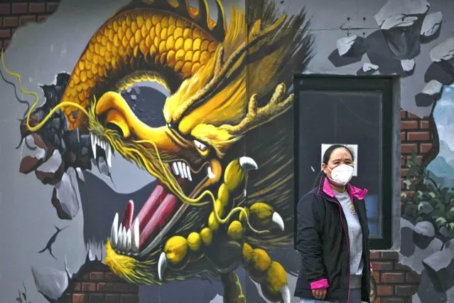 A woman wearing a face mask stands near a mural depicting a dragon in Beijing, Wednesday, November 23, 2022. The latest wave of outbreaks is prompting major cities including Beijing to close off populous districts, shut stores and offices and order factories to isolate the workforces from outside contact. (Photo by Andy Wong/AP Photo)