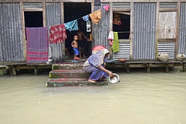 A woman washes her cooking pot in the flood waters outside her house in Sreenagar on July 20, 2020. The death toll from heavy monsoon rains across South Asia has climbed to nearly 200, officials said on July 19, as Bangladesh and Nepal warned that rising waters would bring further flooding. (Photo by Munir Uz Zaman/AFP Photo)