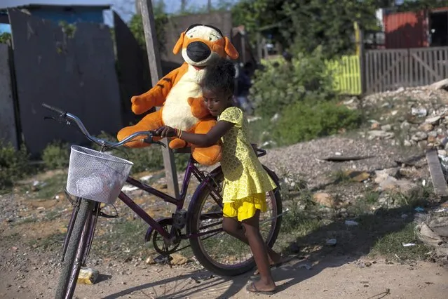A girl pushes on a bike her brand new Tigger plush toy that she received at a foods and toys donation holiday event organized by the non-governmental organization SOMOS, that work to combat hunger, at the Jardim Gramacho favela, in Rio de Janeiro, Brazil, Sunday, December 11, 2020. (Photo by Bruna Prado/AP Photo)