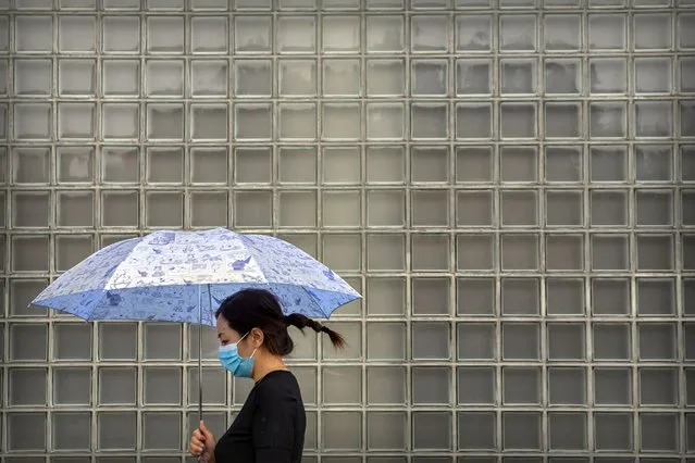 A woman wearing a face mask to protect against the coronavirus walks past a shopping mall on a rainy day in Beijing, Wednesday, September 23, 2020. Even as China has largely controlled the outbreak, the coronavirus is still surging across other parts of the world. (Photo by Mark Schiefelbein/AP Photo)