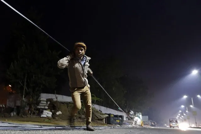 A worker pulls an optic fibre cable to be laid underground along a roadside during the early morning in the western Indian city of Ahmedabad December 23, 2014. (Photo by Amit Dave/Reuters)