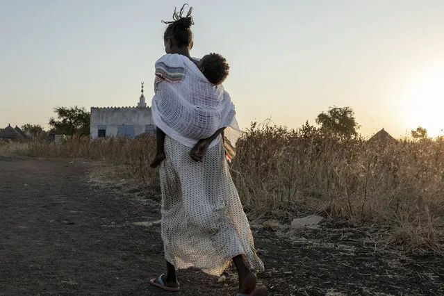 A Tigrayan woman who fled the conflict in Ethiopia's Tigray region, carries her baby to attend Sunday Mass at a church, near Umm Rakouba refugee camp in Qadarif, eastern Sudan, November 29, 2020. (Photo by Nariman El-Mofty/AP Photo)