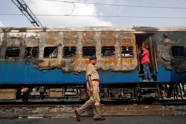 A police officer walks past a damaged coach of a passenger train after it caught fire at a railway station in Mumbai, India, May 29, 2018. (Photo by Francis Mascarenhas/Reuters)