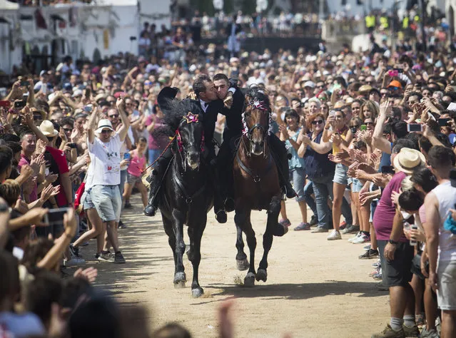 Two riders kiss while galloping during the traditional San Juan (Saint John) festival in the town of Ciutadella, on the Balearic Island of Menorca on June 24, 2018, on the eve of Saint John's Day. During the island's San Juan Festival, held each year on June 23 and 24, Minorcan racehorses gallop and prance on their hind legs through the streets of Ciutadella in honour of the town's patron saint. As the “caixers” (horse riders) ride together in a parade, spectators attempt to pat the horses' chests to get good luck. (Photo by Jaime Reina/AFP Photo)