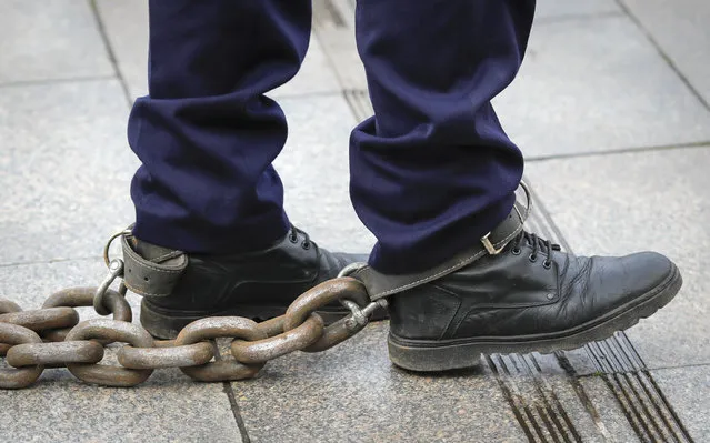 Ioan Canarau, the Vice President of Europol police union walks with chains tied to his feet during a rally in Bucharest, Romania, Thursday, March 25, 2021. Hundreds of police and retired military unionists gathered outside the Ministry of Internal Affairs in the capital where they honked horns, blew whistles, and let off smoke-bombs in the colors of the Romanian flag, as they expressed anger over a two-year salary freeze, pension cuts, and poor working conditions. (Photo by Vadim Ghirda/AP Photo)