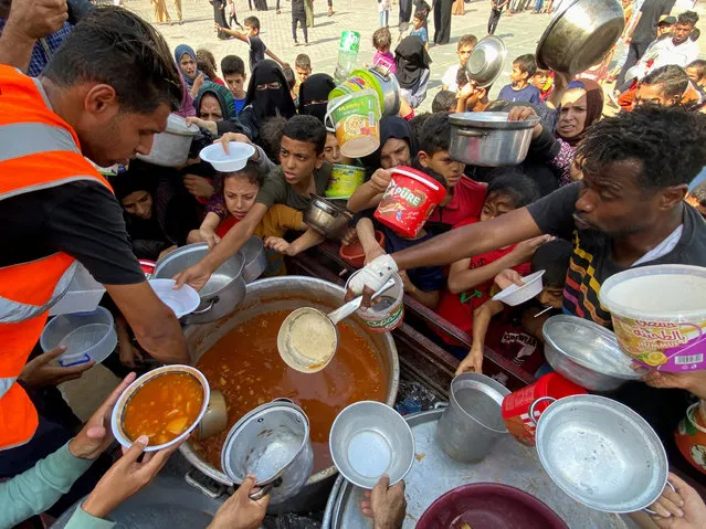 Palestinians, who fled their houses due to Israeli strikes, gather to get their share of charity food offered by volunteers, amid food shortages, at a UN-run school where they take refuge, in Rafah, in the southern Gaza Strip on October 23, 2023. (Photo by Mahmoud al-Masri/Reuters)