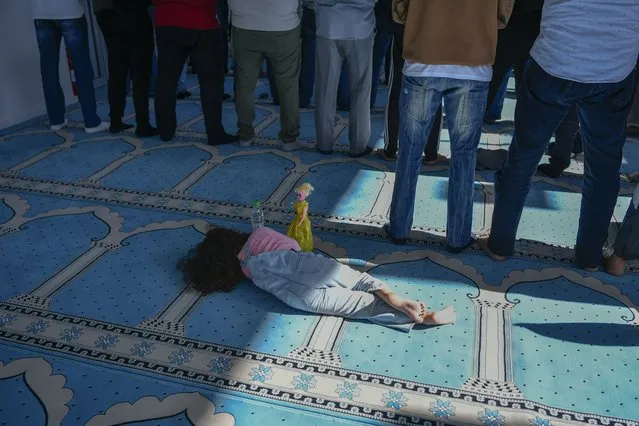 A girl lies on the floor as men pray in a mosque in Athens, Greece, Friday, October 13, 2023. In Muslim communities across the world, worshippers gathered at mosques for their first Friday prayers since Hamas militants attacked Israel, igniting the latest Israel-Hamas war. (Photo by Michael Varaklas/AP Photo)