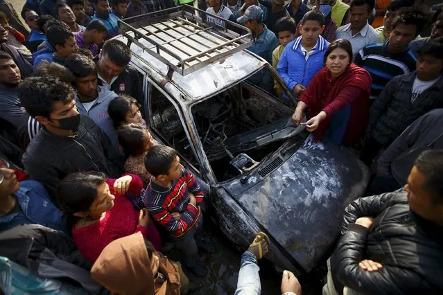 People gather around a taxi burnt by protesters during a nationwide strike organised by the opposition alliance led by the Unified Communist Party of Nepal (Maoist), to demand the new constitution be drafted with the consensus of all political parties, in Kathmandu April 7, 2015. (Photo by Navesh Chitrakar/Reuters)