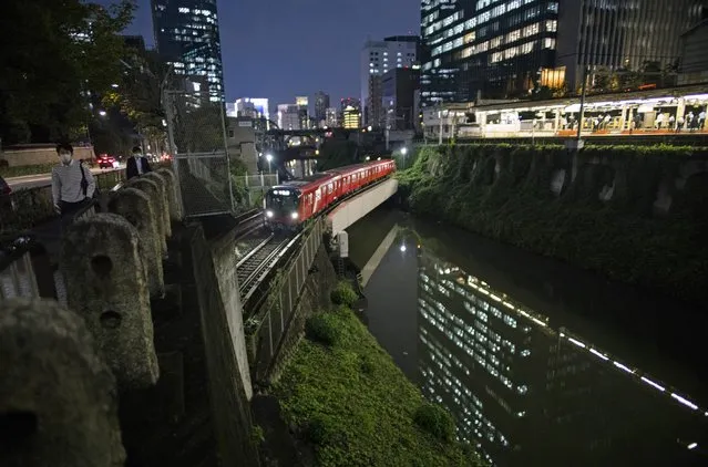 People wearing face masks walk along the Kanda River as a train passes by near a station in Tokyo, Thursday, September 9, 2021. Japan announced Thursday it is extending a coronavirus state of emergency in Tokyo and 18 other areas until the end of September as health care systems remain under severe strain, although new infections have slowed slightly. (Photo by Hiro Komae/AP Photo)