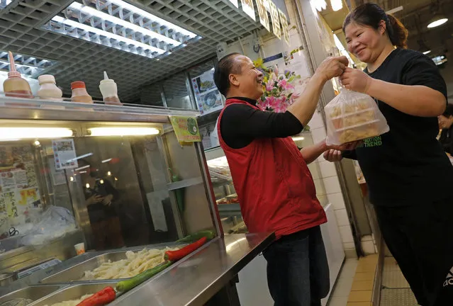 In this Monday, Jan. 23, 2017 photo, chicken feet snacks shop owner Leung Kin-kung, left, hands chicken feet takeaway to a customer in Hong Kong. Saturday marks the start of the lunar Year of the Rooster and families in China will reunite for festivities, fireworks and food. While tradition calls for feasting on “auspicious” foods, many will also munch on staple snacks like “phoenix claws,” the Chinese name for chicken feet. (AP Photo/Vincent Yu)
