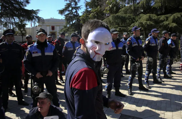 A protester wearing a mask walks near police guarding the parliament building, as thousands of opposition supporters protest in Tirana, Albania on Saturday, March 16, 2019. Albanian opposition supporters clashed with police while trying to storm the parliament building Saturday in a protest against the government which they accuse of being corrupt and linked to organized crime. (Photo by Visar Kryeziu/AP Photo)