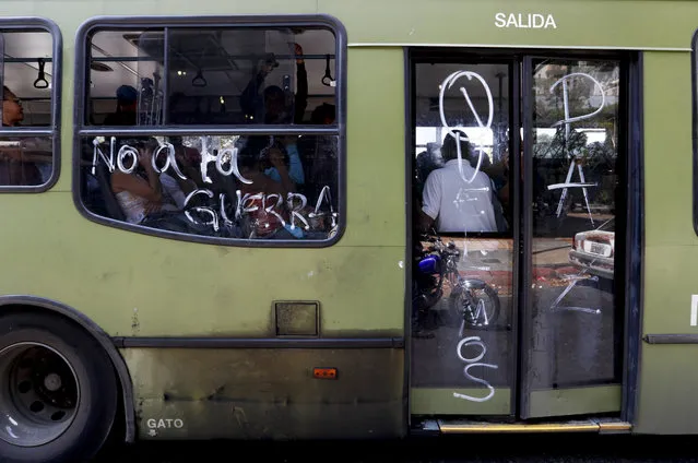 Passengers ride on a bus with messages scrawled on it that read in Spanish “No to war”, and “We want peace”, in Caracas, Venezuela, Thursday, March 14, 2019. With long lines at the stops of public transport and crowds of people at the entrance of some banking agencies, Venezuelans returned to activity on Thursday after four days of paralysis as a result of the biggest blackout in the country's history. (Photo by Eduardo Verdugo/AP Photo)
