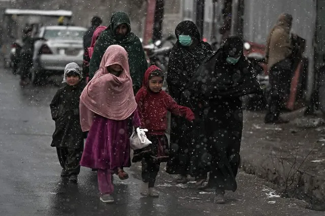 Women and children walk along a road during the first snow in Kabul on December 15, 2021. (Photo by Mohd Rasfan/AFP Photo)