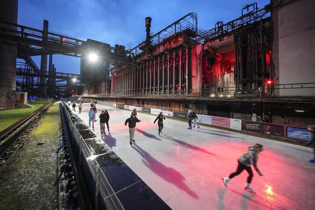 People skating on ice at the illuminated former coking plant Zollverein in Essen, Germany, Monday, December 11, 2023. The World Heritage site once was the hottest place in town, where coke was made at 1,000 degrees Celsius, now the industrial landmark becomes an ice rink every winter for the citizens. (Photo by Martin Meissner/AP Photo)