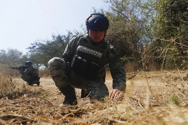 Mexican Army soldiers demonstrate a search for anti-personnel mines during a media presentation near Naranjo de Chila in the municipality of Aguililla, Mexico, Friday, February 18, 2022. The town had been the scene of a bloody turf battle between two drug cartels. Earlier this month the government sent a large army contingent to free the zone from organized crime. (Photo by Armando Solis/AP Photo)