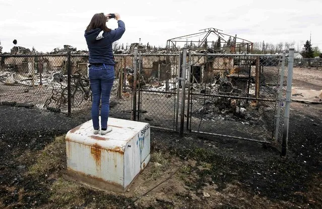A woman takes photos of the burned remains of a house in the Abasand neighbourhood of Fort McMurray, Alberta, Canada, May 9, 2016 after wildfires forced the evacuation of the town. (Photo by Chris Wattie/Reuters)