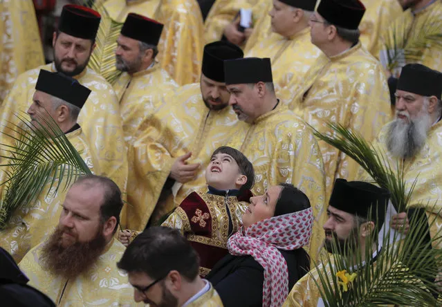 In this Saturday, April 8, 2017, picture a Romanian Orthodox priest's son looks up along with his mother during a service ahead of Palm Sunday in Bucharest, Romania. (Photo by Vadim Ghirda/AP Photo)