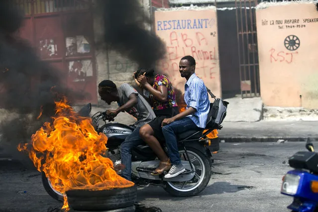 A moto-taxi driver takes two passengers past a burning barricade set up by people protesting fuel shortages in Port-au-Prince, Haiti, Monday, September 16, 2019. Haiti was at a standstill Monday with no public transportation available and closed banks, government offices, and schools amid street protests due to a fuel crisis. (Photo by Dieu Nalio Chery/AP Photo)