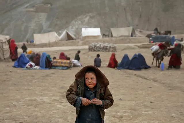 In this Sunday, May 4, 2014 photo, an Afghan child protects himself from the rain, near the site of Friday's landslide that buried Abi-Barik village in Badakhshan province, northeastern Afghanistan. Stranded and with no homes, many of the families have struggled to get aid. Some have gone to nearby villages to stay with relatives or friends, while others have slept in tents provided by aid groups. The unlucky ones have slept outside. (Photo by Massoud Hossaini/AP Photo)