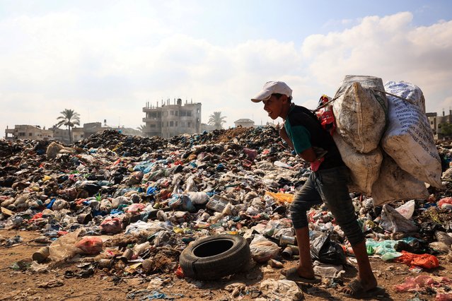 A Palestinian youth carrying sacks of salvagable items walks past piles of waste, as garbage collection and any other municipality services come to a halt due to the Israeli bombardment of the Gaza Strip, at the al-Maghazi Palestinian refugee camp, in the central Gaza Strip on July 15, 2024, amid the ongoing conflict between Israel and the Palestinian Hamas militant group. (Photo by Eyad Baba/AFP Photo)