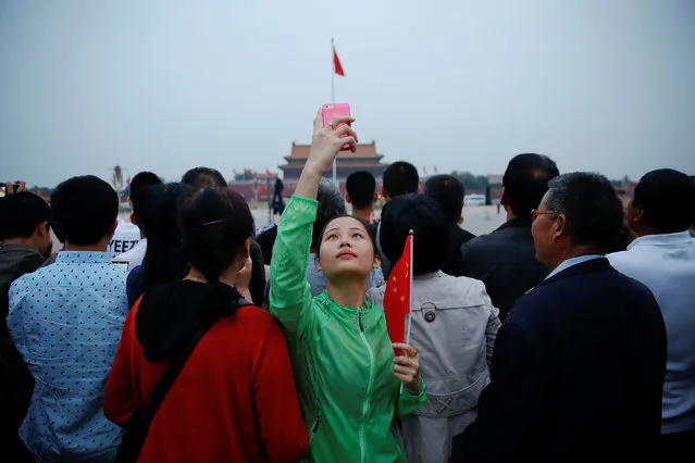 A girl holds a Chinese flag and takes picture of herself as people gather for a flag-raising ceremony at the Tiananmen Square in Beijing, China June 4, 2016. (Photo by Damir Sagolj/Reuters)