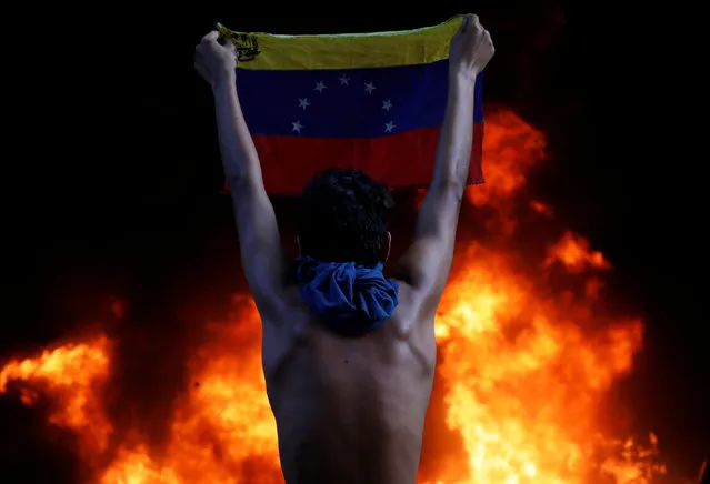 A protester holds a national flag as a bank branch, housed in the magistracy of the Supreme Court of Justice, burns during a rally against Venezuela's President Nicolas Maduro, in Caracas, Venezuela June 12, 2017. (Photo by Carlos Garcia Rawlins/Reuters)