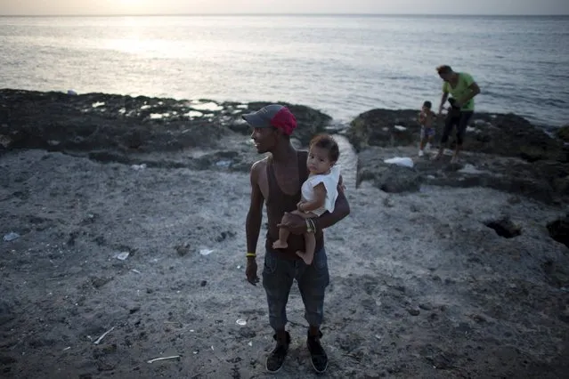 School worker Ivan Gago, 33, holds his 5 months old son as he watches the sunset in Havana, August 5, 2015. (Photo by Alexandre Meneghini/Reuters)