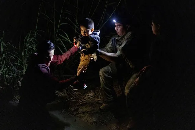 A member of the Texas Army National Guard helps grab two year old Juan Miguel of Guatemala from David, an asylum seeking migrant from Ecuador, after the migrants used a raft to cross the Rio Grande river into the United States from Mexico in Roma, Texas, June 9, 2022. (Photo by Adrees Latif/Reuters)