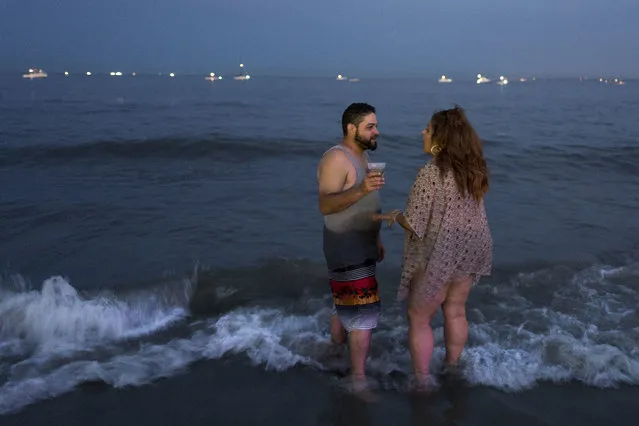 In this July 21, 2017 photo, a couple cools their feet in the Coney Island surf in New York. Coney Island is a storied place, known for Nathan’s hot dogs, old-fashioned amusement park rides and a gritty beach. But after sundown it has a different feel. With the crowds and tourists mostly gone, locals come out to enjoy balmy summer evenings as the heat of the day subsides. (Photo by Mark Lennihan/AP Photo)