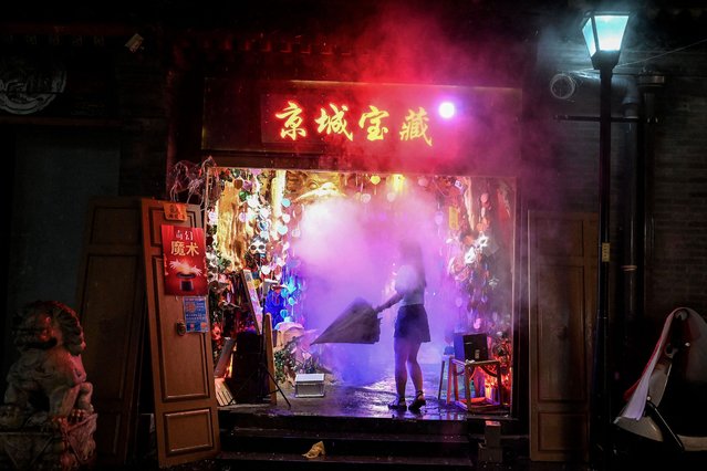 A woman folds an umbrella to enter a gift shop in Nanlouguxiang Alley during a rainfall in Beijing on July 27, 2022. (Photo by Noel Celis/AFP Photo)