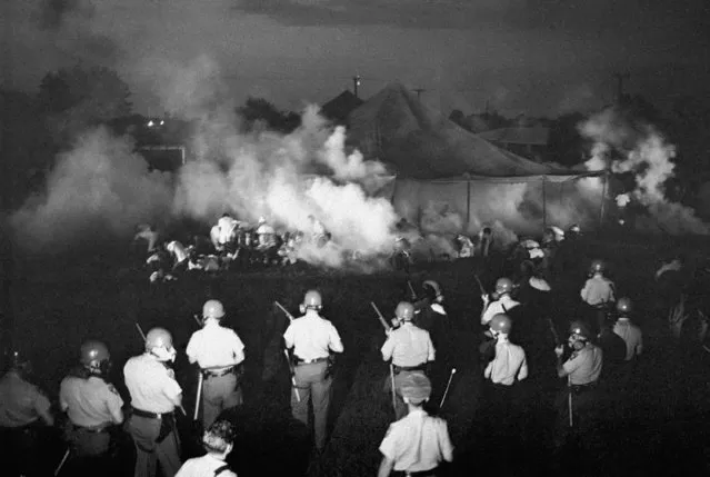In this June 23, 1966 file photo, Mississippi Highway Patrolmen and Canton Police officers wearing gas masks, foreground, advance after firing tear gas into one of the Meredith marchers' tents in Canton, Miss. The action took place in a schoolyard which the civil rights demonstrators chose as a campsite after being turned away earlier. (Photo by Charles Kelly/AP Photo)