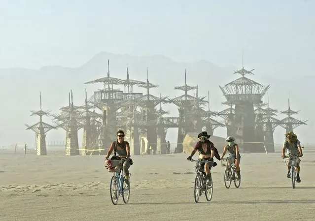 A group of burners ride their bikes as the sun sets on a dusty afternoon on Nevada's Black Rock Desert during Burning Man on Saturday, August 27, 2022. The 2022 Burning Man theme is Waking Dream. (Photo by Andy Barron/The Reno Gazette-Journal via AP Photo)
