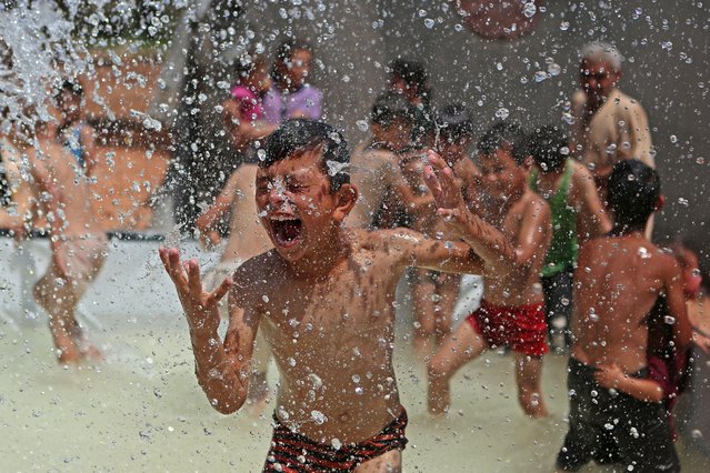 A Syrian boy reacts as he gets sprayed with water in a portable swimming pool set up by volunteers, at a camp for the displaced in the rebel-held town of Kafr Yahmul in the northern countryside of Idlib on August 10, 2022. (Photo by Aaref Watad/AFP Photo)