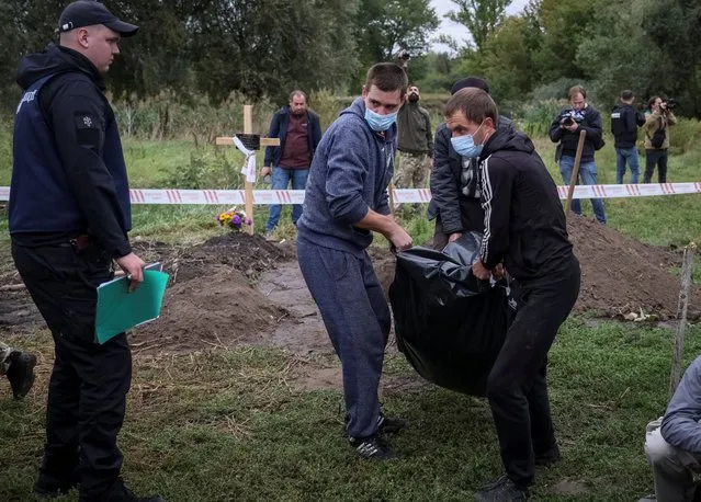 A police officer looks on as workers carry the body of a person who, according to Ukrainian police, was killed by Russian troops during Russia's invasion, in the town of Balakliia, recently liberated by Ukrainian Armed Forces, in Kharkiv region, Ukraine on September 13, 2022. (Photo by Gleb Garanich/Reuters)