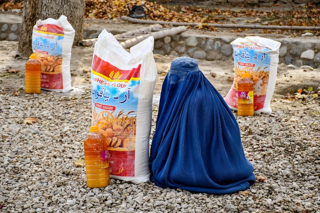 An Afghan burqa-clad woman sits next to food aid distributed by a local charity foundation in Mazar-i-Sharif on December 10, 2024. (Photo by Atif Aryan/AFP Photo)